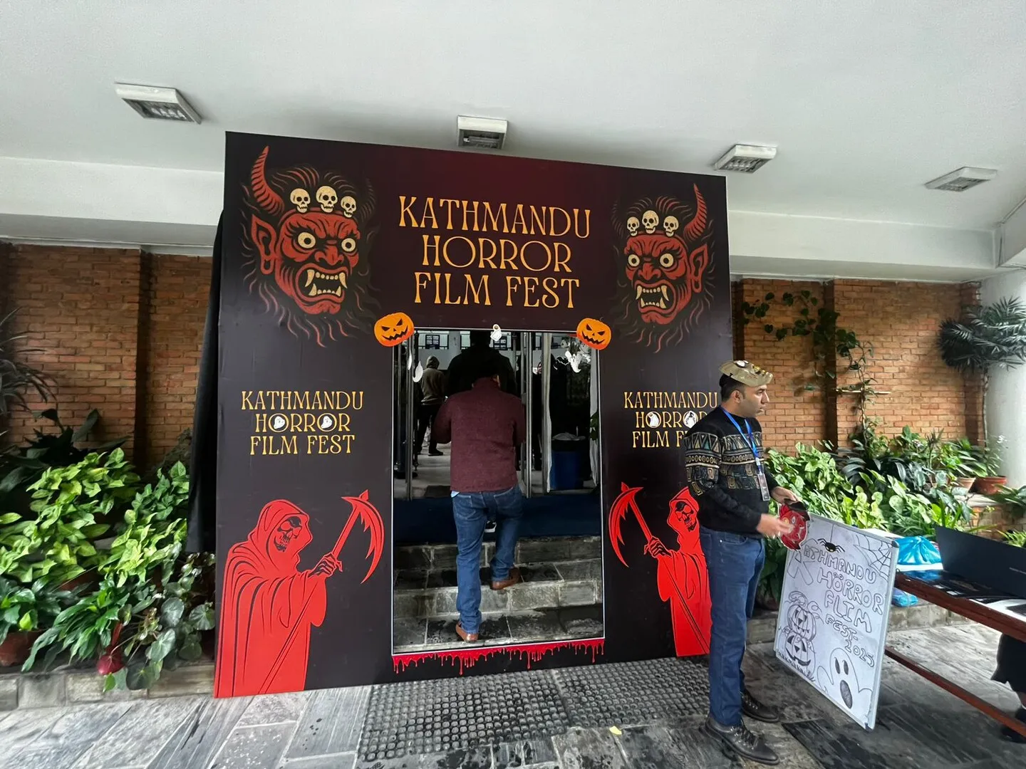 Festival entrance at Kathmandu Horror Film Fest, with a painted backdrop of red masked deities and reapers flanking the doorway