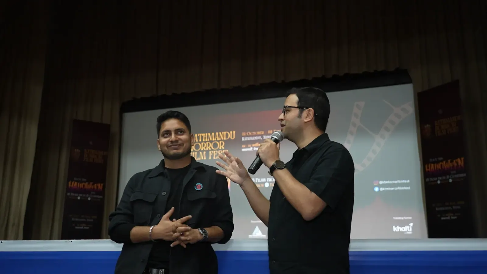 Two filmmakers taking questions on stage in front of the festival screen